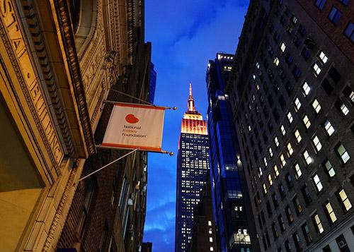 NKF office sign in front of the Empire State Building, which is lit up in orange lights for National Kidney Month
